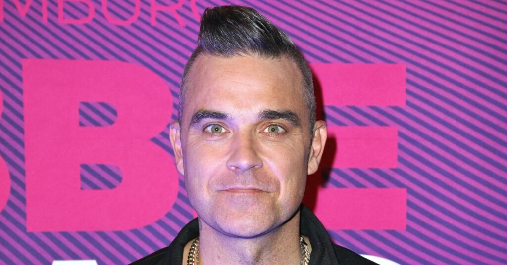 Robbie Williams stands against a purple background
