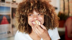 A woman smiles while eating a sandwich