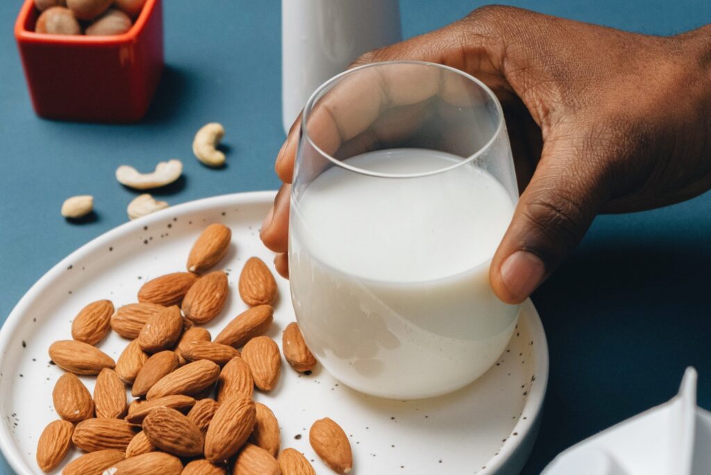 Photo of a hand holding a glass of almond milk on a plate full of almonds