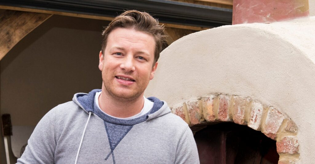 Jamie Oliver stood in front of a pizza oven