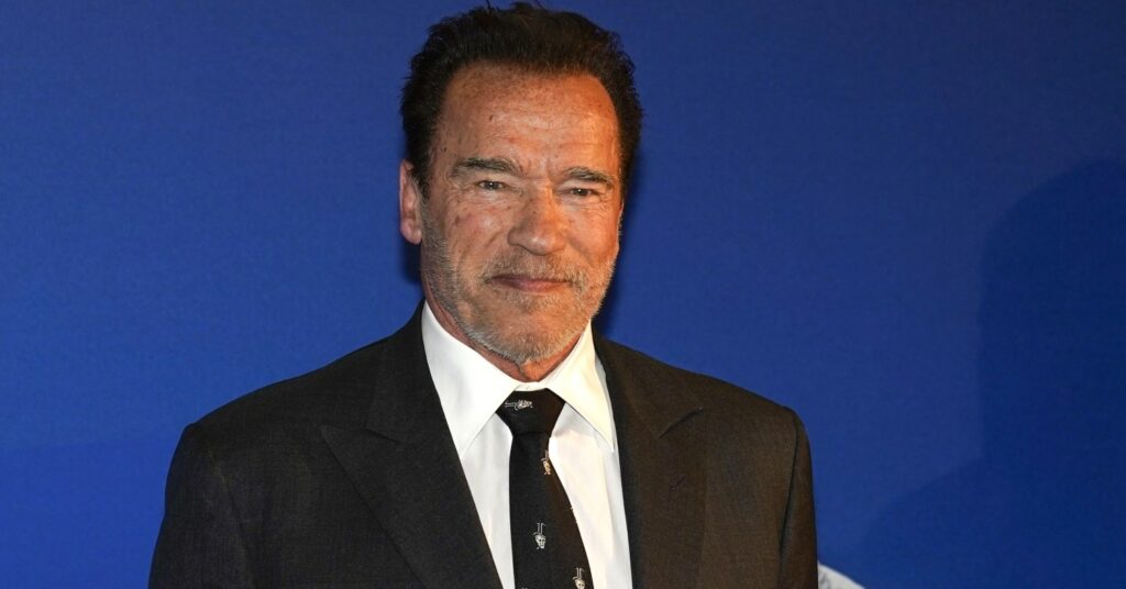 Arnold Schwarzenegger stands against a blue background