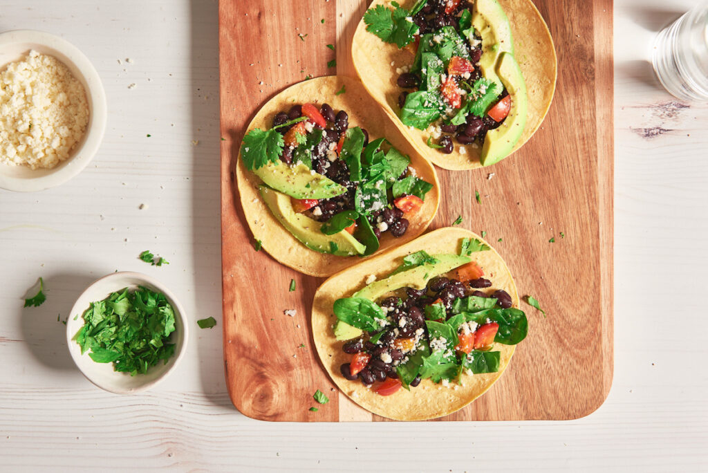 Photo shows three black bean tacos with fresh salad on a wooden board. Vegetarian food is a not a modern invention, and the diet's history goes back thousands of years.