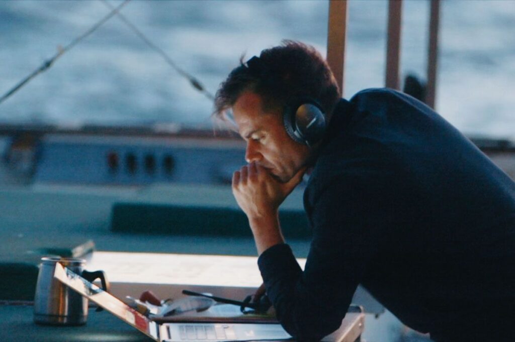 Director Joshua Zeman looking at a laptop with headphones on, on a boat during his search for the loneliest whale.