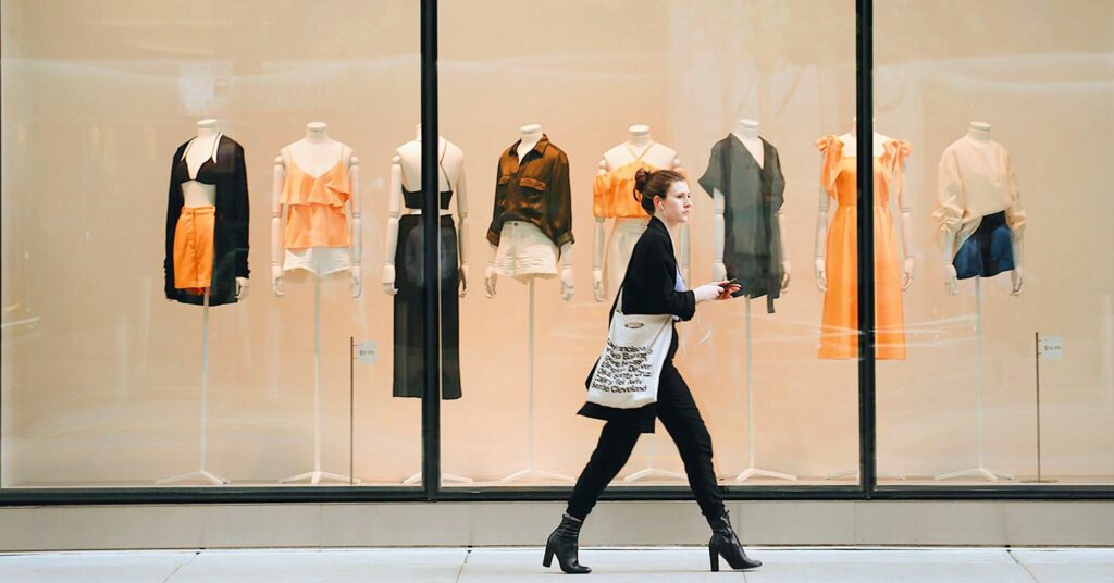 A woman walks down a high street past a clothing store