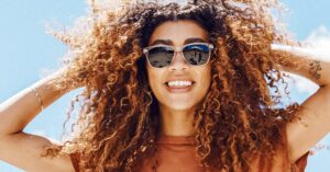 a woman with curly hair smiles wearing Sunski sunglasses wearing