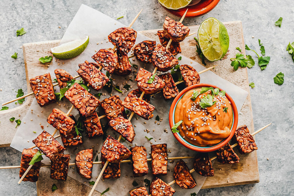 Photo of tempeh skewers alongside dip and cut limes.