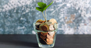 Photo features a small glass filled with small change with a green plant growing out of it. Today, impact investing is for everyone, even beginners.