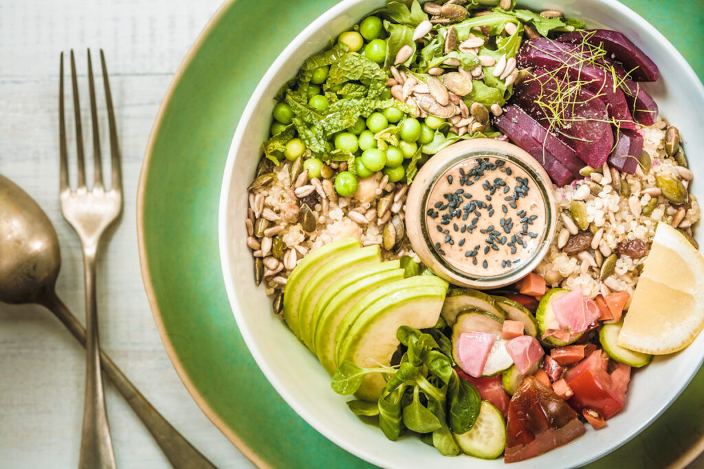 Photo shows a salad bowl featuring avocado, grains, seeds, and greens with a small dish of peanut and miso sauce. Eating a plant-based diet has a variety of different science-backed health benefits.
