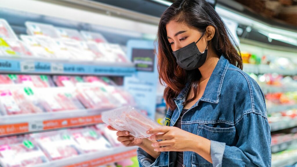 A woman looking at a packet of bacon in the supermarket.