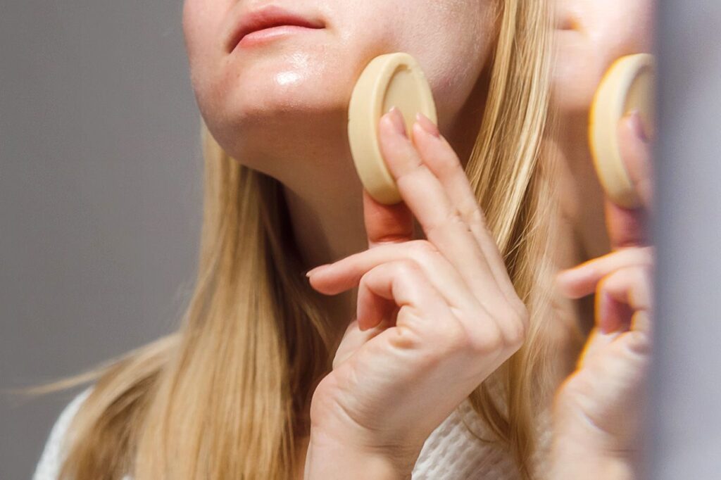 A white woman with blonde hair holds a cleansing bar to her face