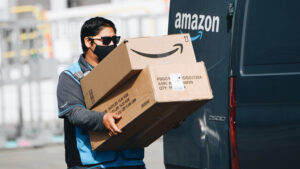 Photo shows an Amazon delivery driver loading branded boxes into a van. Amazon and several other companies just pledged to use 100 percent zero carbon shipping by 2040.
