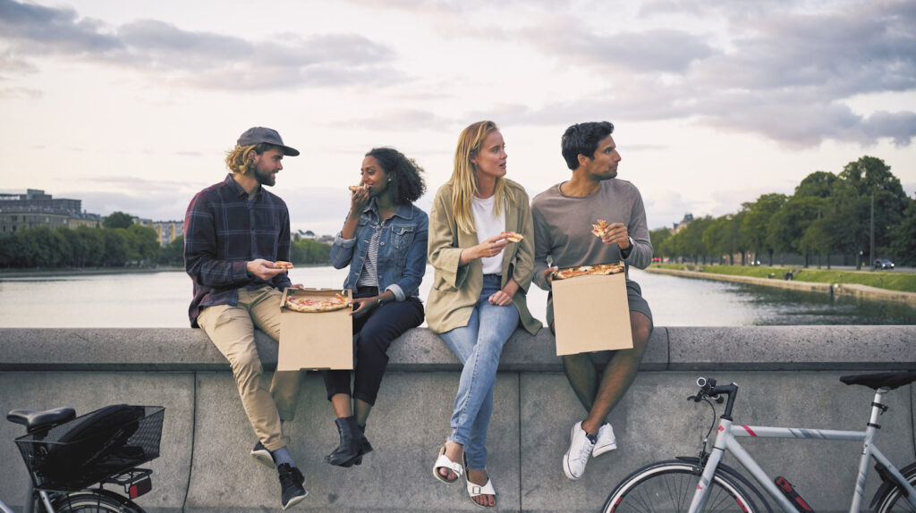 Photo shows a group of young people eating together outside next to a lake. Denmark's new climate plan aims to tackle the impact of climate change through food.