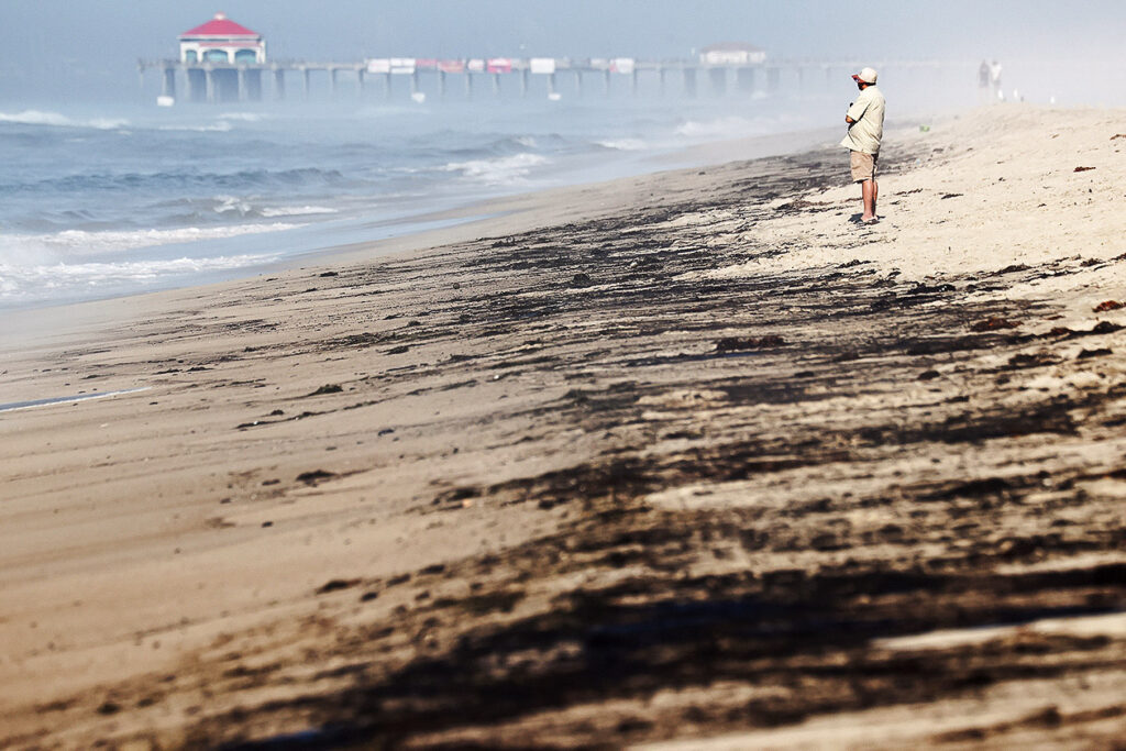 Photo shows someone standing on a beach with what appears to be tar-like stains on the sand.