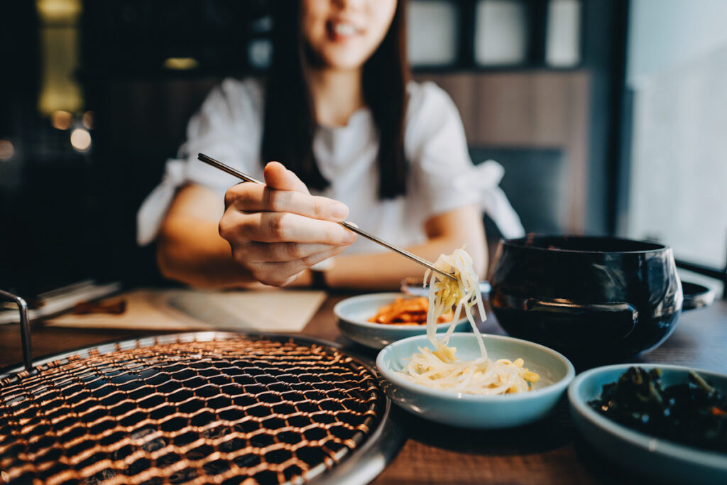 Photo shows a young Asian woman eating a beansprout-based Korean appetitizer.