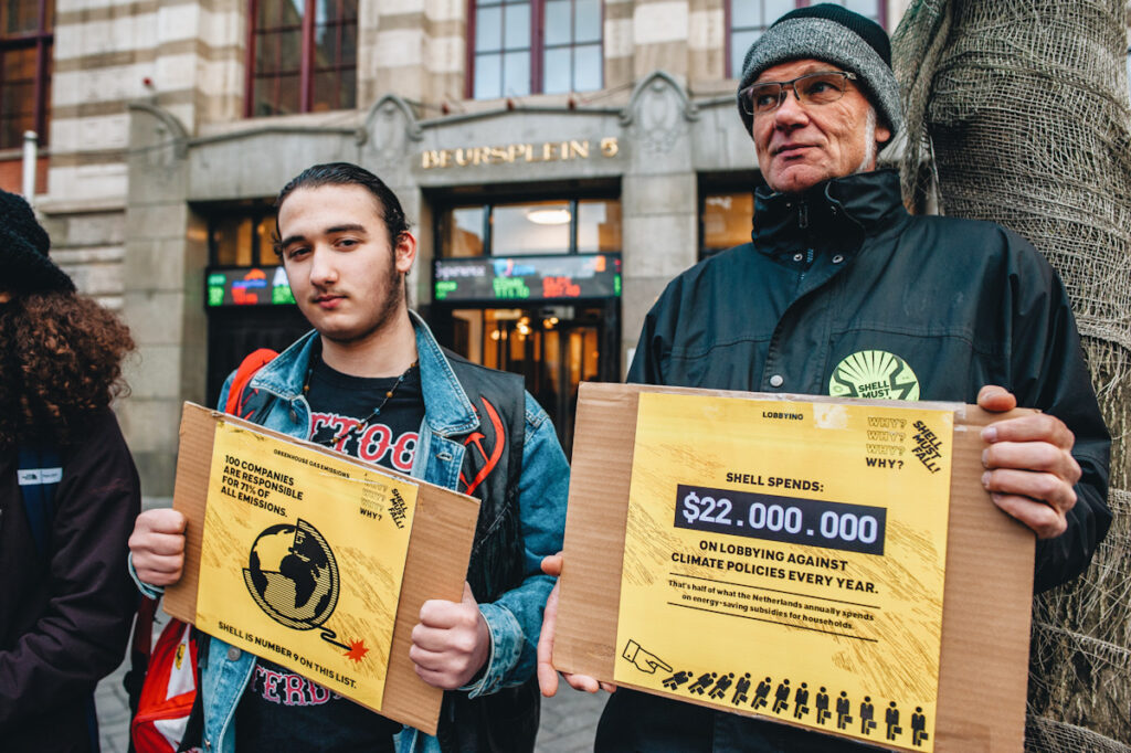 Photo shows two activists holding placards at a protest in front of the Amsterdam stock exchange last year, protesting Shell. Big Oil is finally on trial.