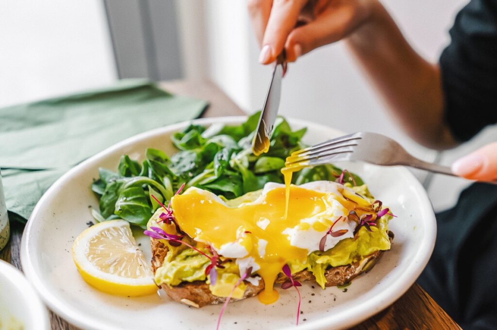 Photo shows real egg on toast along with a fresh salad, lemon, and avocado.