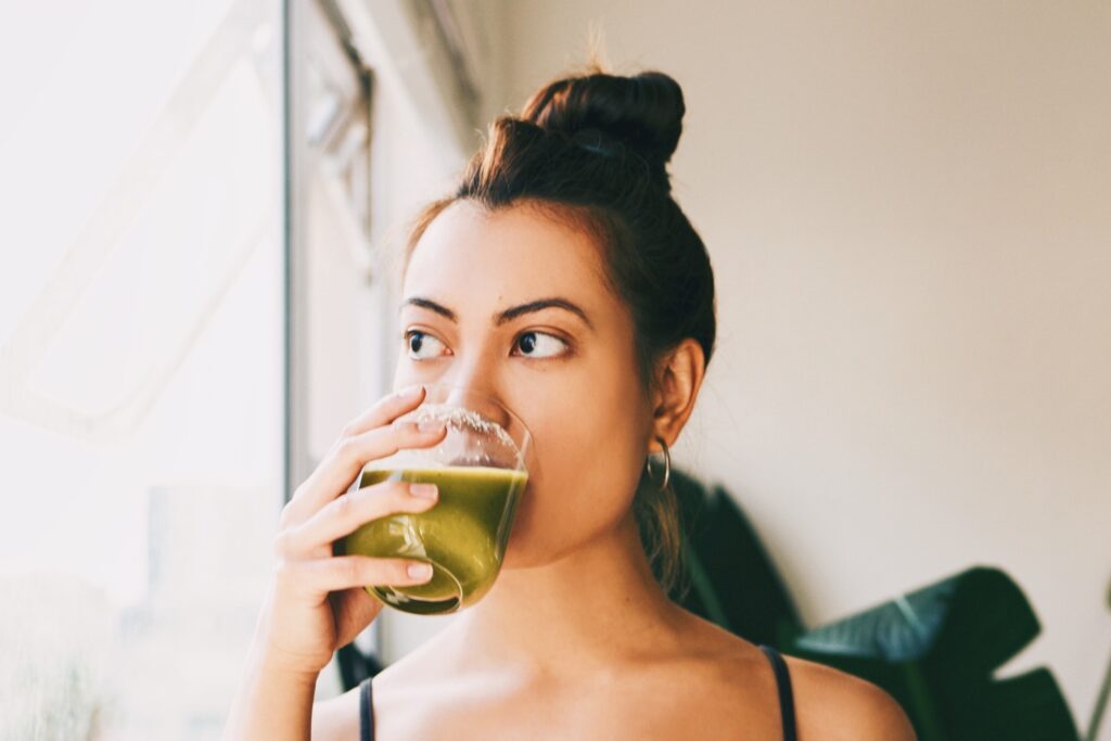 Photo shows a woman drinking a green smoothie.