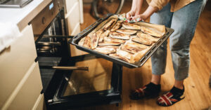Photo shows someone taking a sheet pan of baked and glazed aubergine out of the oven.