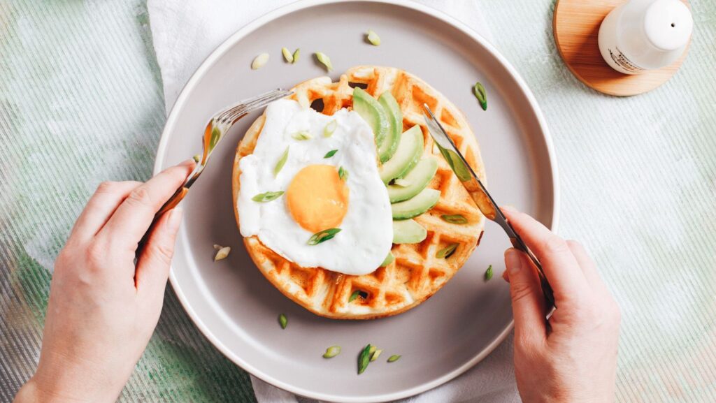 Photo shows a waffle topped with a sunnyside up egg.