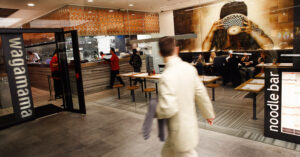 Photo shows a customer walking past the clear glass front of a Wagamama restaurant.
