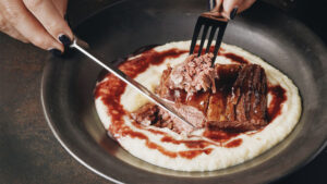Photo shows a knife and fork cutting into Redefine Meat's 3D printed beef steak, showing the fibrous, hard-to-replicate grains synonymous with traditional animal protein.