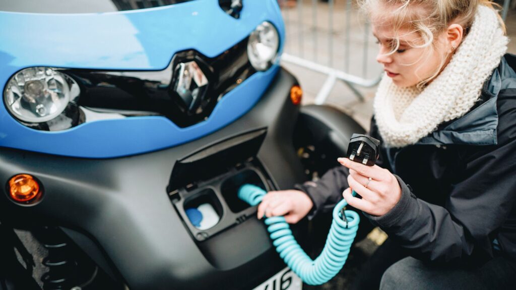 A woman kneels next to an electric car holding a charger