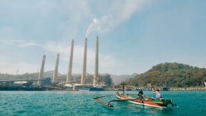 fishermen on a boat as smoke rises from Cilegon's Suralaya coal power plant.