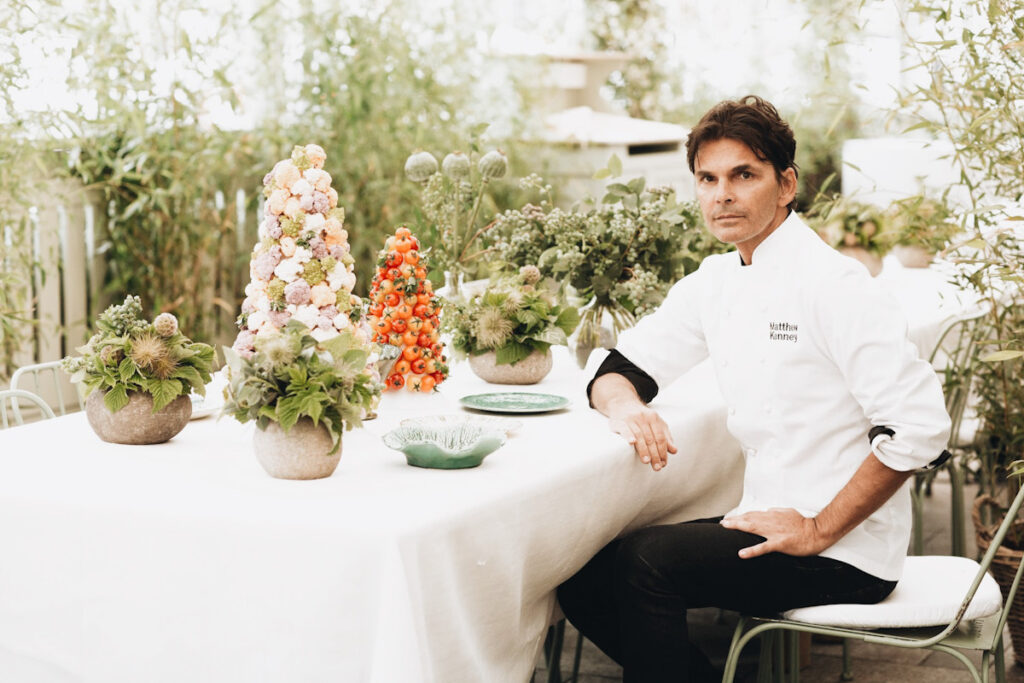 Photo shows chef Matthew Kenney sat at a white table elaborately decorated with flowers.