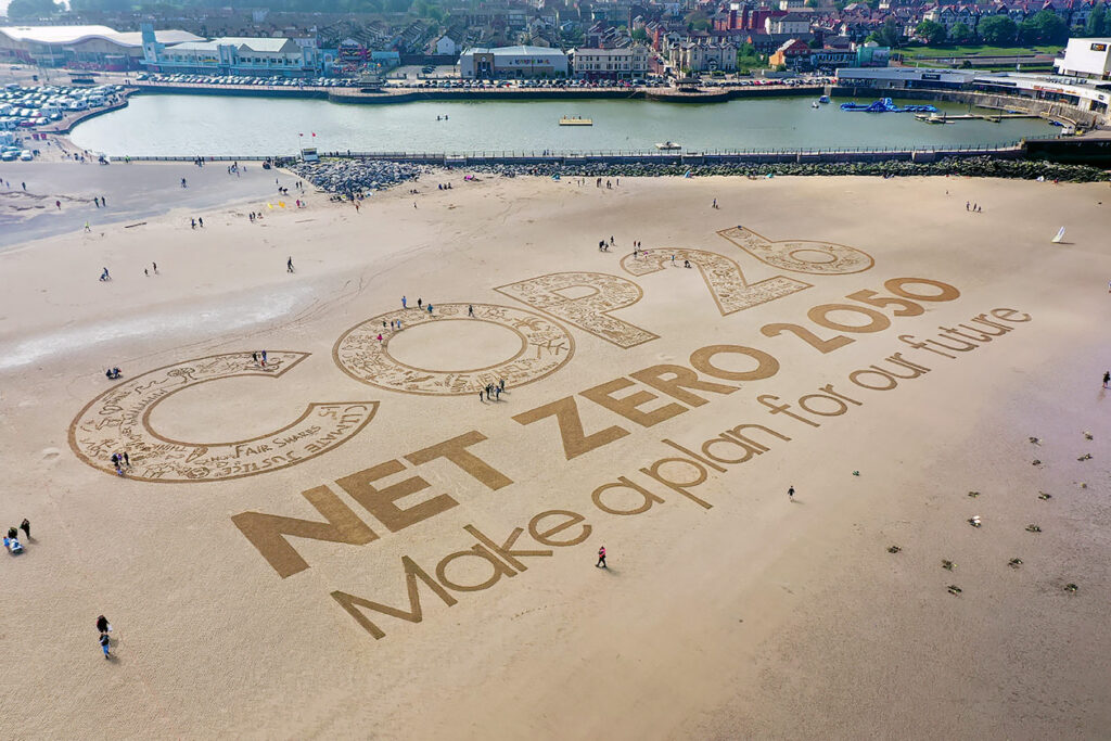 Photo shows a beach with words written in the sand. They say: "COP26 Net Zero 2050, Make a plan for our future."