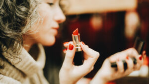 Photo shows a woman putting on lipstick using a hand-held compact mirror. New Jersey just passed a ban on cosmetic animal testing.