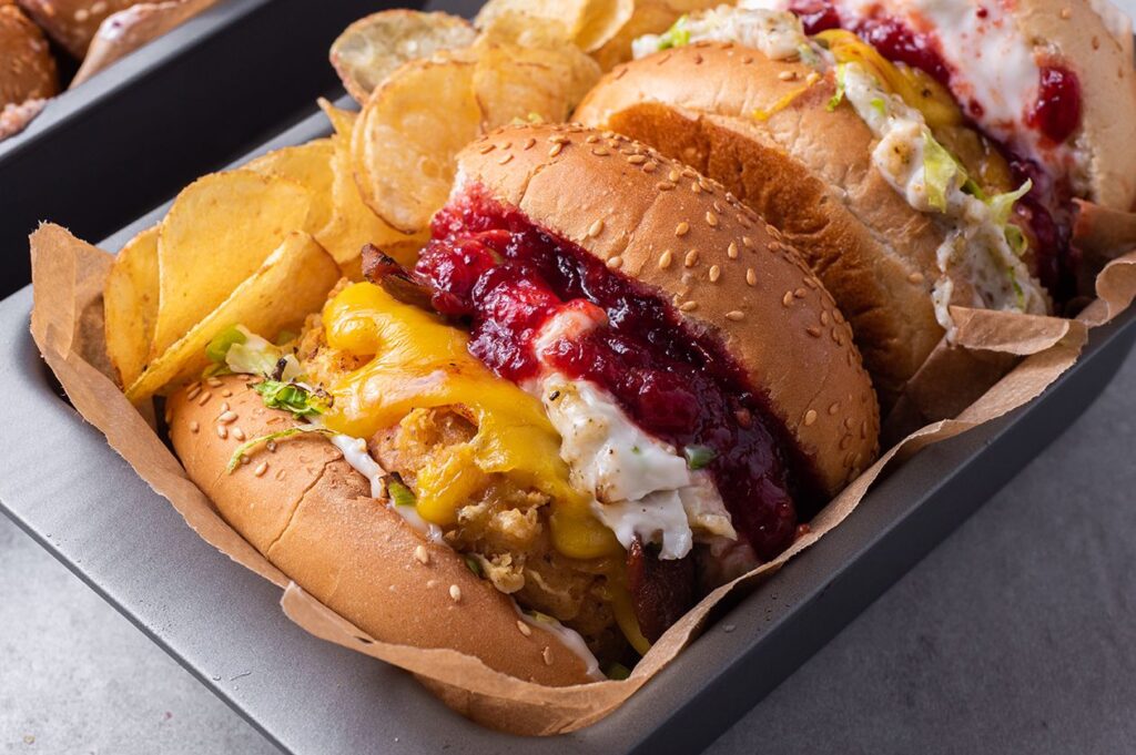 Photo shows a sandwich featuring a crispy vegan chicken patty, dairy-free cheese, and cranberry ketchup on a burger bun