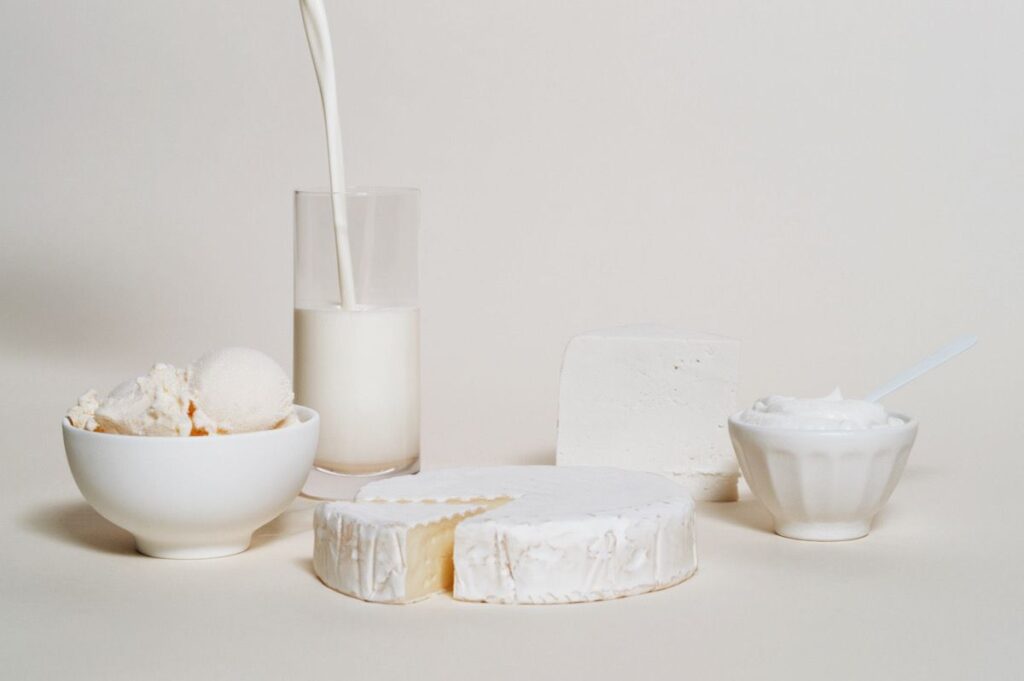 Photo shows various dairy products, like milk, brie, and ice cream, on a white background