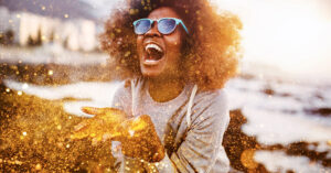 Photo shows a woman scooping a double handful of gold glitter which blows around the bottom half of the picture. Glitter pollution is a growing problem.