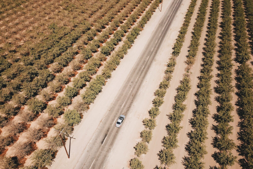 Aeriel image shows a lone car driving on a long stretch of rural road surrounded by crops.