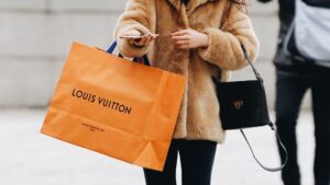 A woman walks along with an orange Louis Vuitton bag