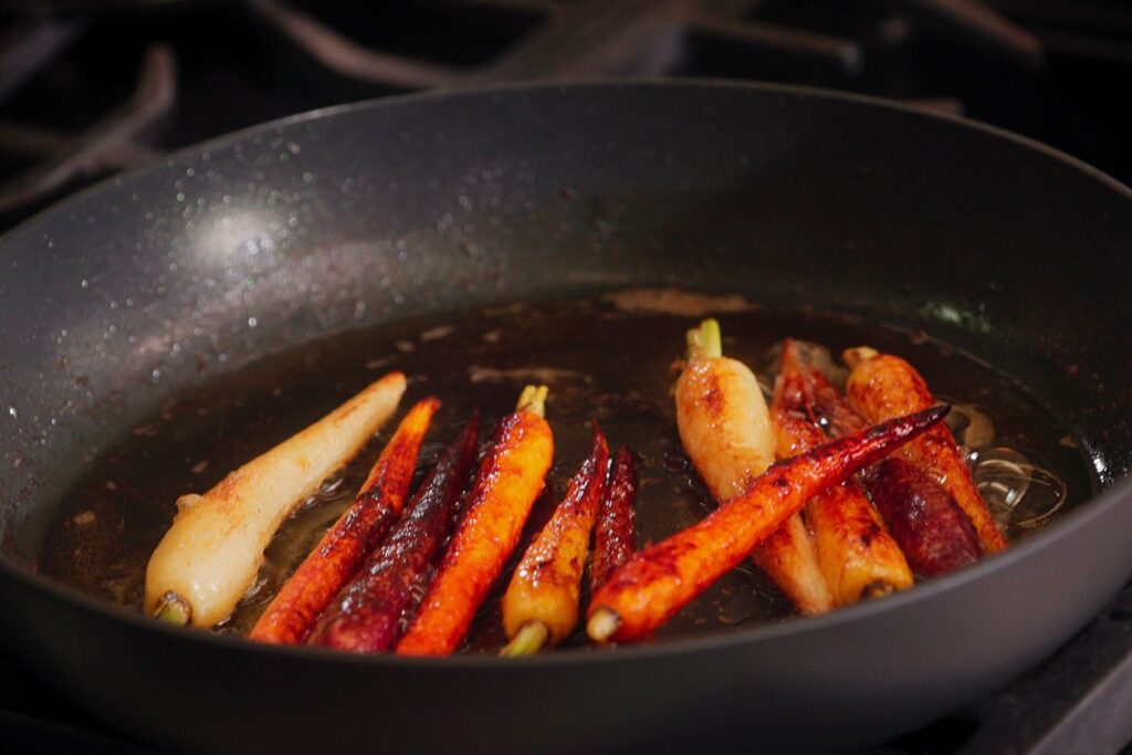 Photo shows rainbow glazed carrots in a cast-iron skillet