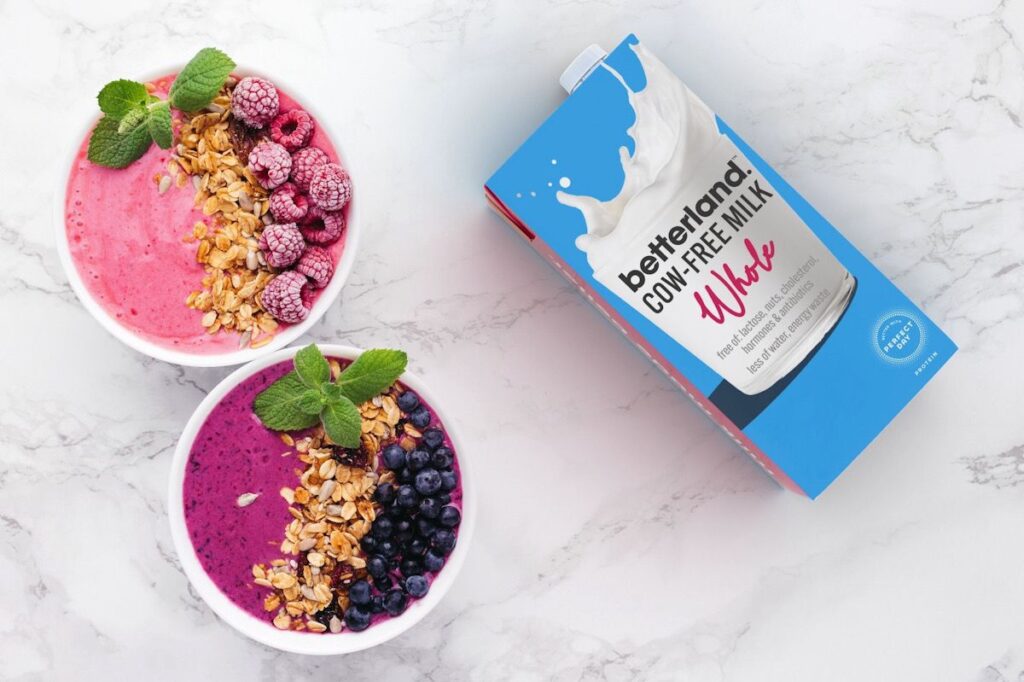 Photo shows a carton of Betterland Foods milk on a marble background next to two smoothie bowls