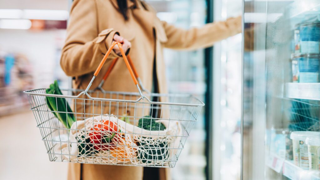 Close up photograph of a woman carrying a shopping basket full of groceries in a supermarket. Is sustainability still just for a privileged few?