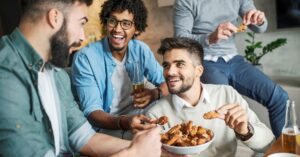Photo shows a group of men eating chicken wings and drinking beer
