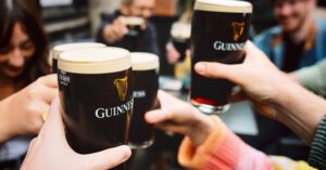 Photo shows a group of people holding their Guinness-branded glasses up in cheers. Guinness is embracing sustainability via regenerative agriculture.