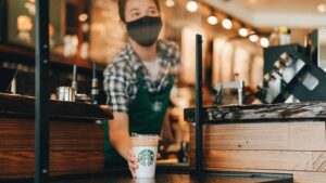 Photo shows a Starbucks barista serving up a coffee in a branded reusable mug rather than a single-use cup.