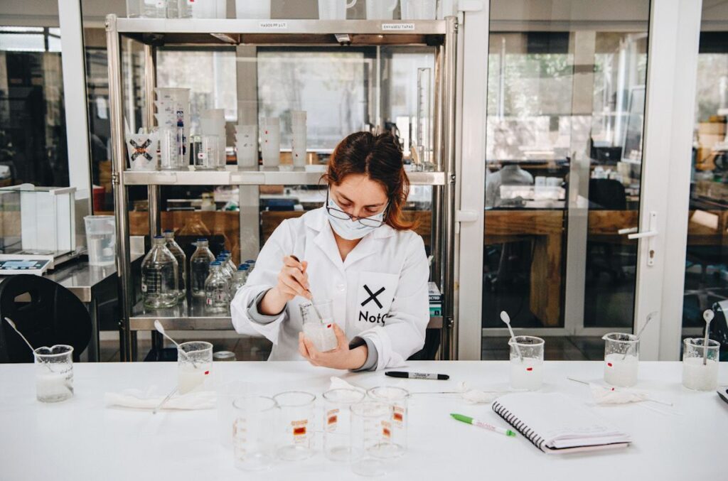 Photo shows a scientist in a white lab coat embroidered with the text "NotCo" on the breast pocket. She is mixing a liquid in a beaker.